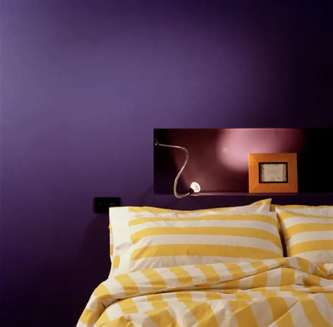 Yellow and white striped pillows and duvet on bed below light on alcove shelf in modern purple bedroom