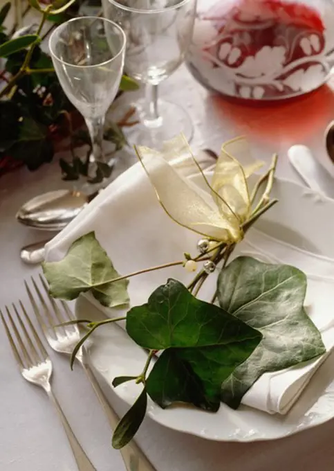 Close-up of green ivy leaves and sprig of mistletoe decorating white plate on Christmas dining table