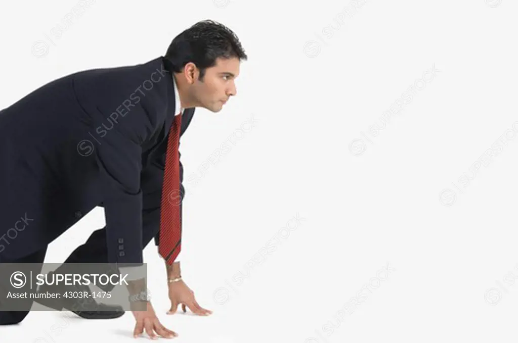 Young businessman kneeling in preparation for race, side view