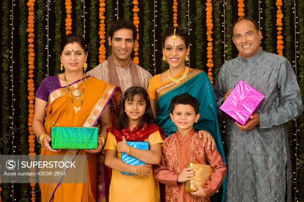 Three generation Indian family holding gifts, background flower background