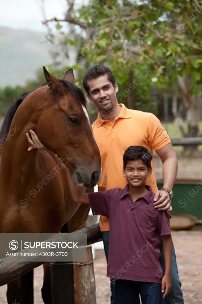 Father and son holding a horse, smiling.