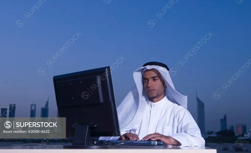 Young Arab man sitting at a desk - office with Dubai City in the background