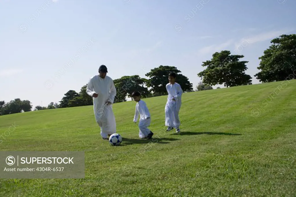 Father with sons playing football in park