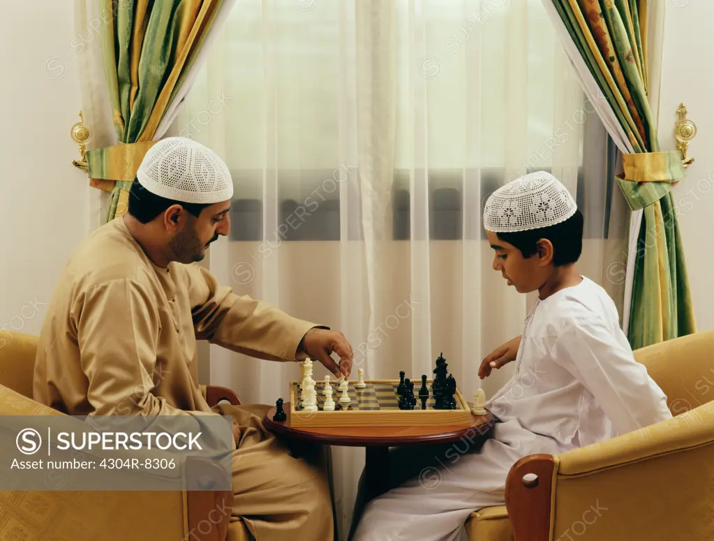 A father and a son playing chess at their residence.