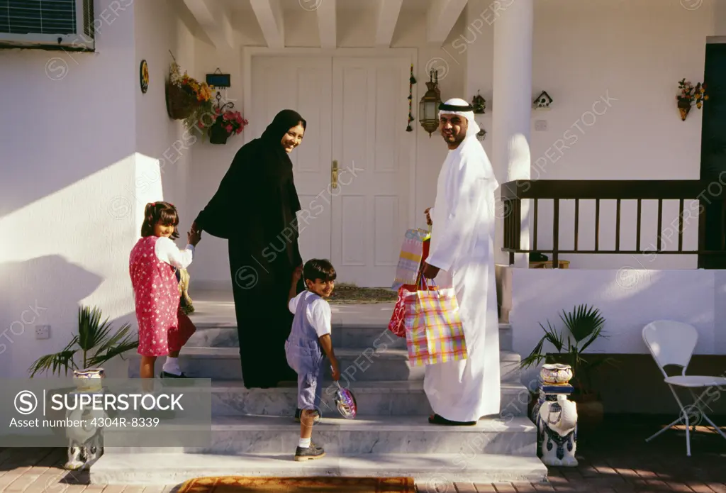 A family turns back and looks at the camera before entering the house.