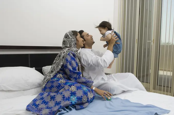 Parents sitting on the bed in the bedroom playing with baby