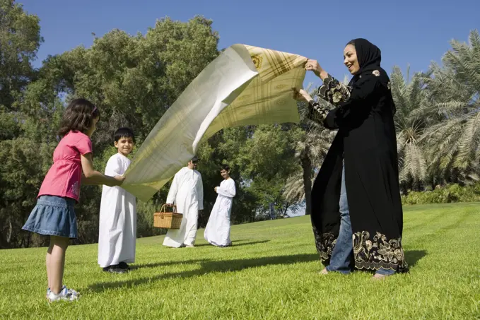 Mother with children spreading sheet on grass while father with son standing in background