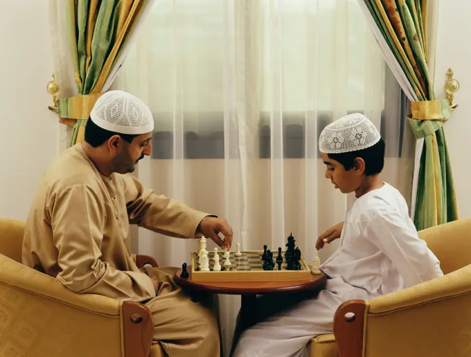 A father and a son playing chess at their residence.