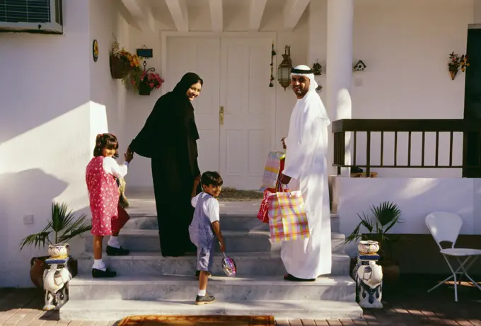 A family turns back and looks at the camera before entering the house.