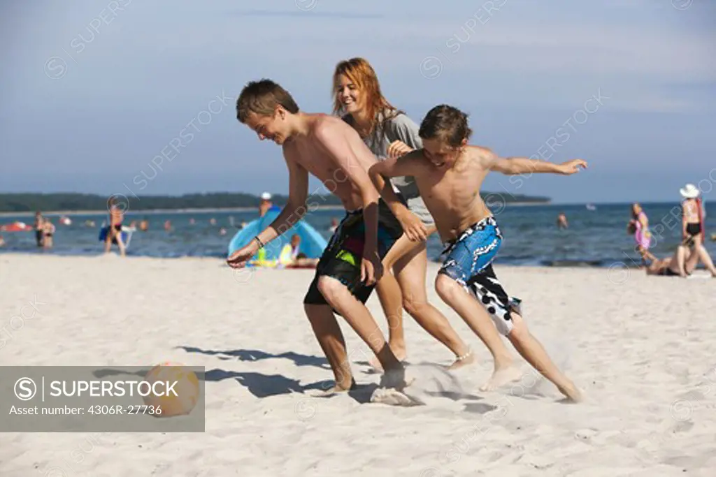 Children playing football on beach with mother