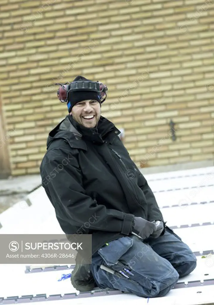 Young construction worker kneeling on roof