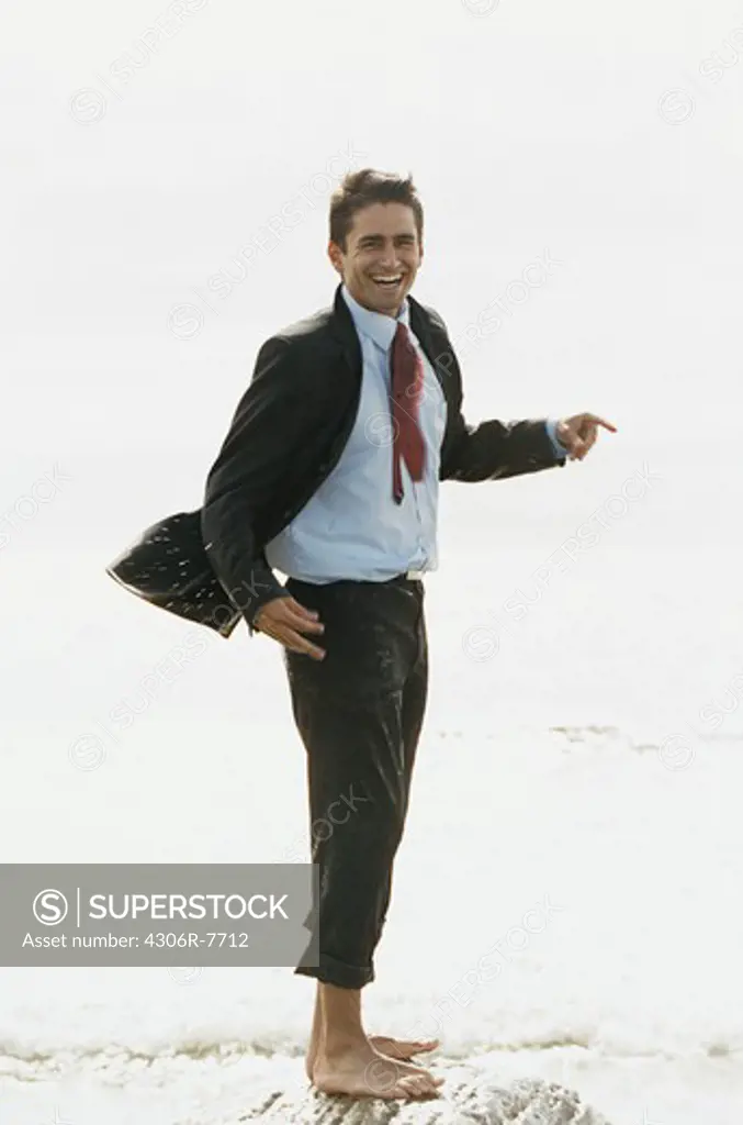 Barefoot businessman standing on rock in sea, laughing