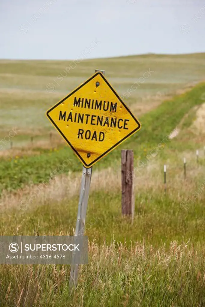 Minimum maintenance road sign in front of a country road completely overgrown by grasslands, Nebraska