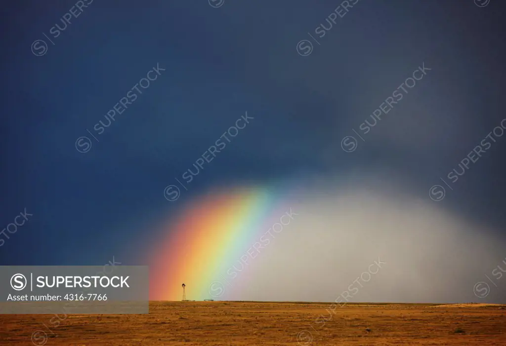 USA, Colorado, Rainbow, and curtains of rain at base of powerful thunderstorm, ending at lone windmill on open plains