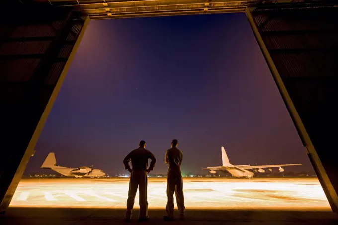 Two United States Marine aviators scan the flight line on which two KC-130J Super Hercules sit parked at Kuantan Air Base, Malaysia.