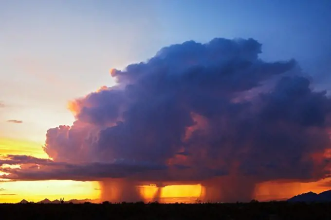 A thunderstorm, or cumulonimbus, unleashes twin curtains of rain over Tucson, Arizona at sunset.