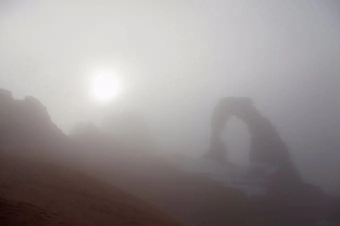 Winter fog visually obscures a view of Delicate Arch, Arches National Park, Utah.