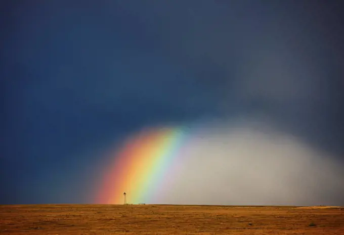 USA, Colorado, Rainbow, and curtains of rain at base of powerful thunderstorm, ending at lone windmill on open plains