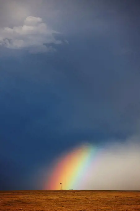 USA, Colorado, Rainbow, and curtains of rain at base of powerful thunderstorm, ending at lone windmill on open plains