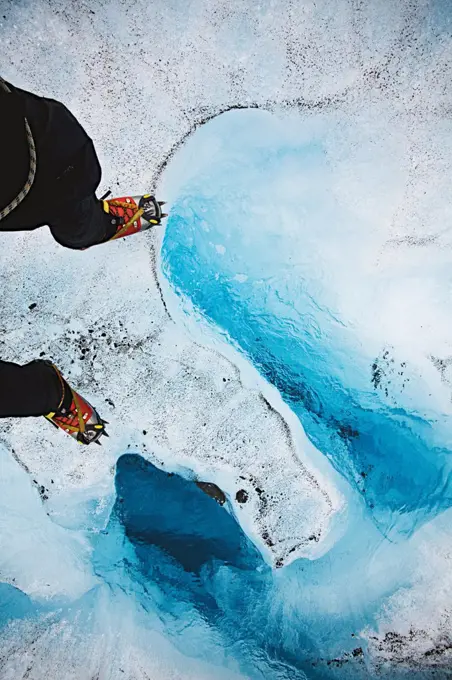 A hiker wearing a pair of crampons walks on top of the Mendenhall Glacier in Juneau, Alaska. The Glacier has many small and large river systems running from within itself.