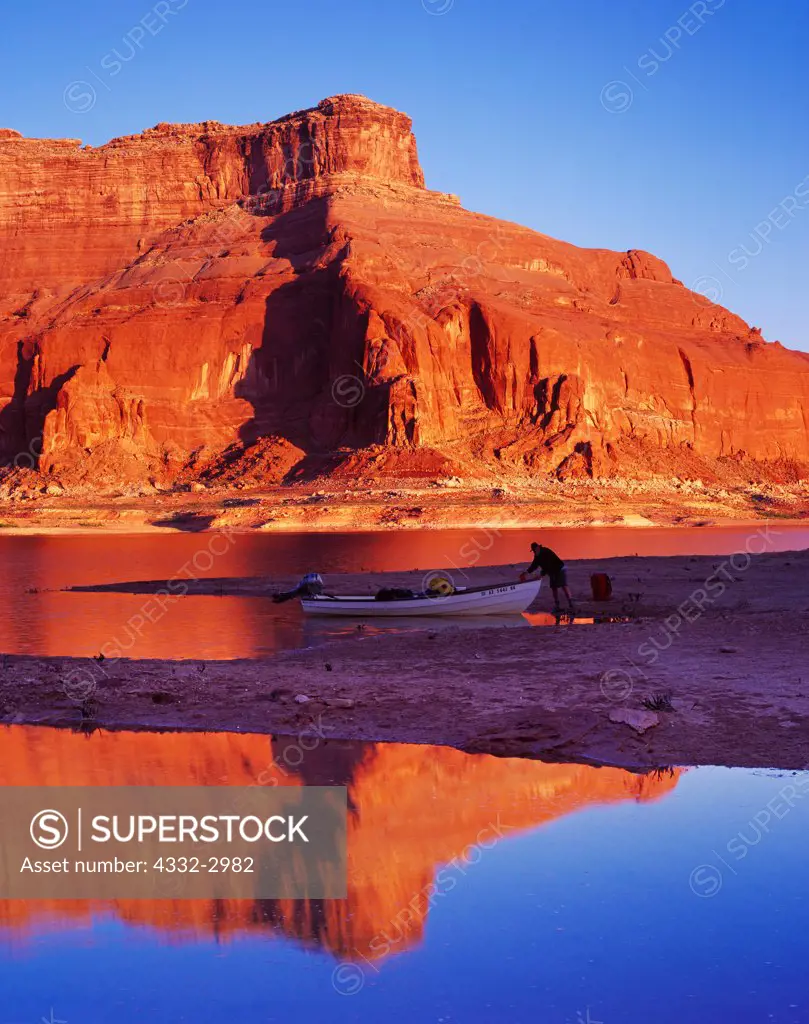 Morning reflection of Tim Pfeiffer loading Bristol Skiff on shore of Lake Powell near mouth of Dungeon Canyon, Glen Canyon National Recreation Area, Utah.