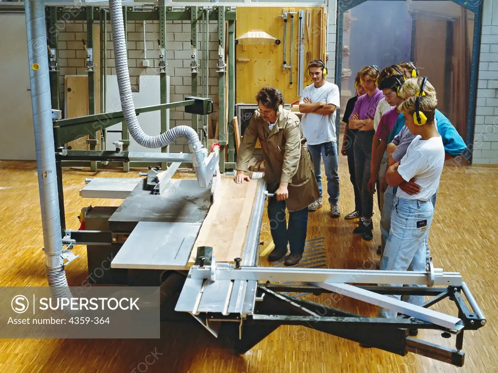 An instructor demonstrating the use of a panel saw for a line of students.