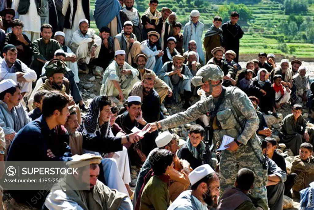 (Kapisa Province, Afghanistan) U.S. Army Spc. Joshua McDaniel with Provincial Reconstruction Team Kapisa passes out flyers written in Dari wishing the people of Kapisa a Happy Ramadan. A crowd from nearby villages gathered to watch a shura (meeting) between village elders and PRT to discuss concerns about road construction near their farmland.