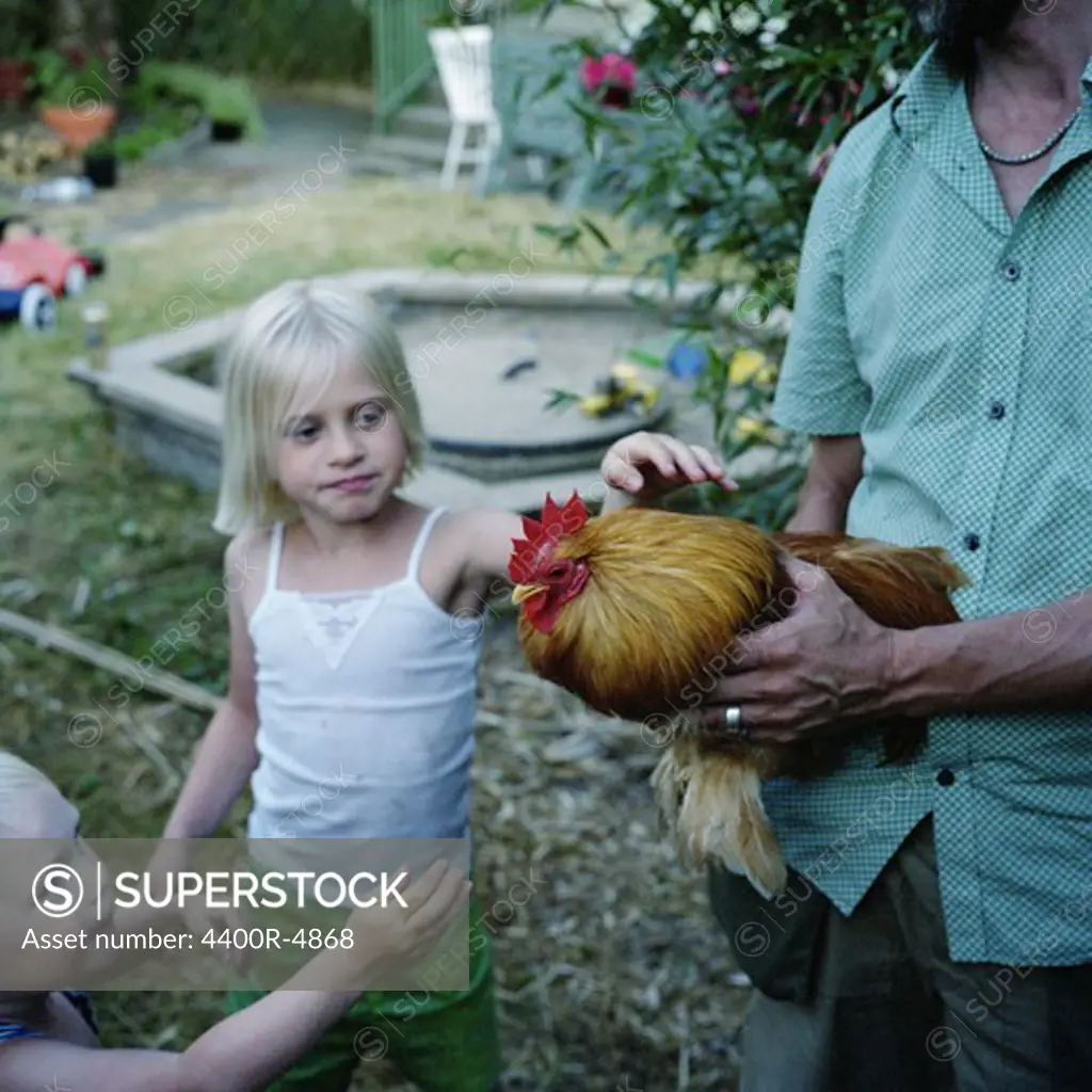 Man holding rooster, children standing beside