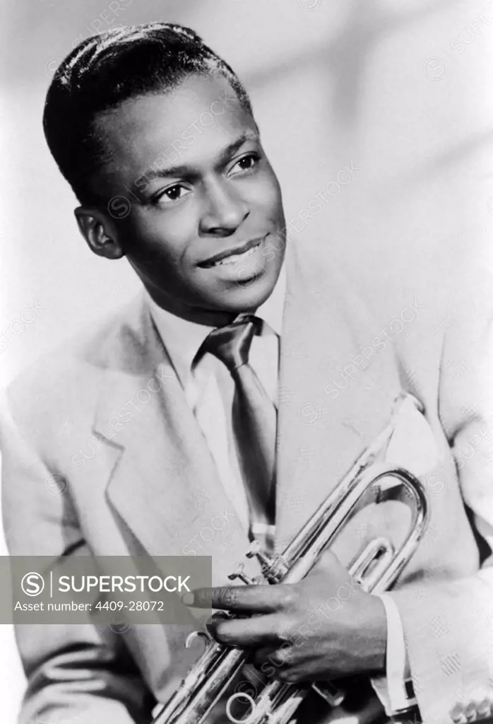 Studio portrait of American jazz trumpeter Miles Davis smiling and holding his trumpet, 1949.