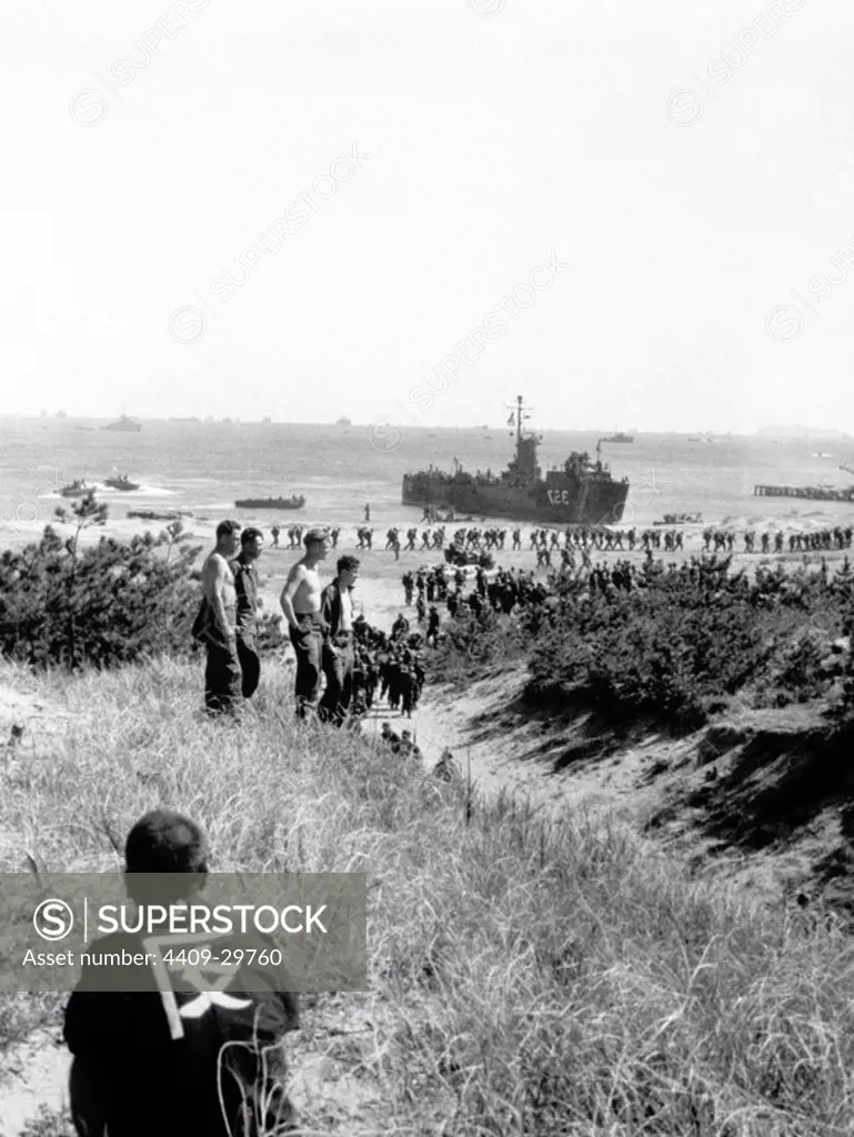 Native japanese sits on his haunches and watches men of the 130th Regt, 33rd Div, make and amphibious landing during "invasion". Japan, 9/2/45.