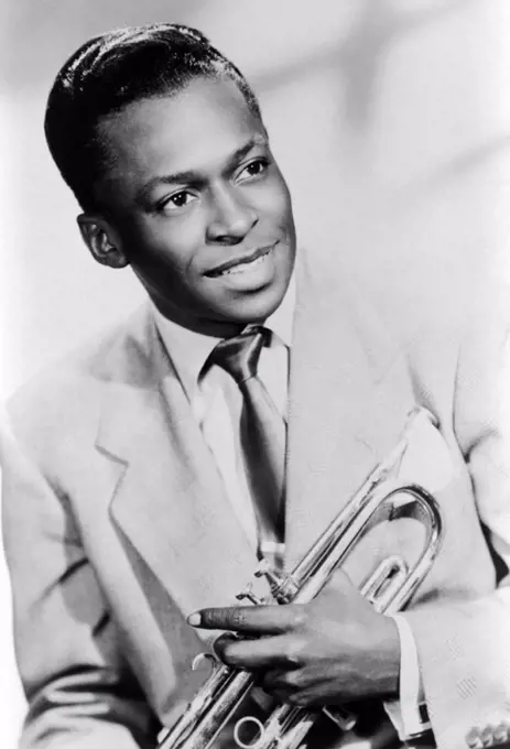 Studio portrait of American jazz trumpeter Miles Davis smiling and holding his trumpet, 1949.