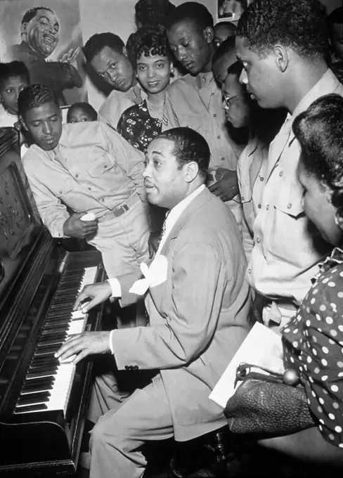 American jazz musician Duke Ellington plays the piano for a group of servicemen and women, Hartford, Connecticut, 1942. Jazz vocalist Joya Sherrill, who sang with Ellington thorughout most of the 1940s, stands at center rear (she wears a pearl neckace). A poster de Ellington is on the wall.