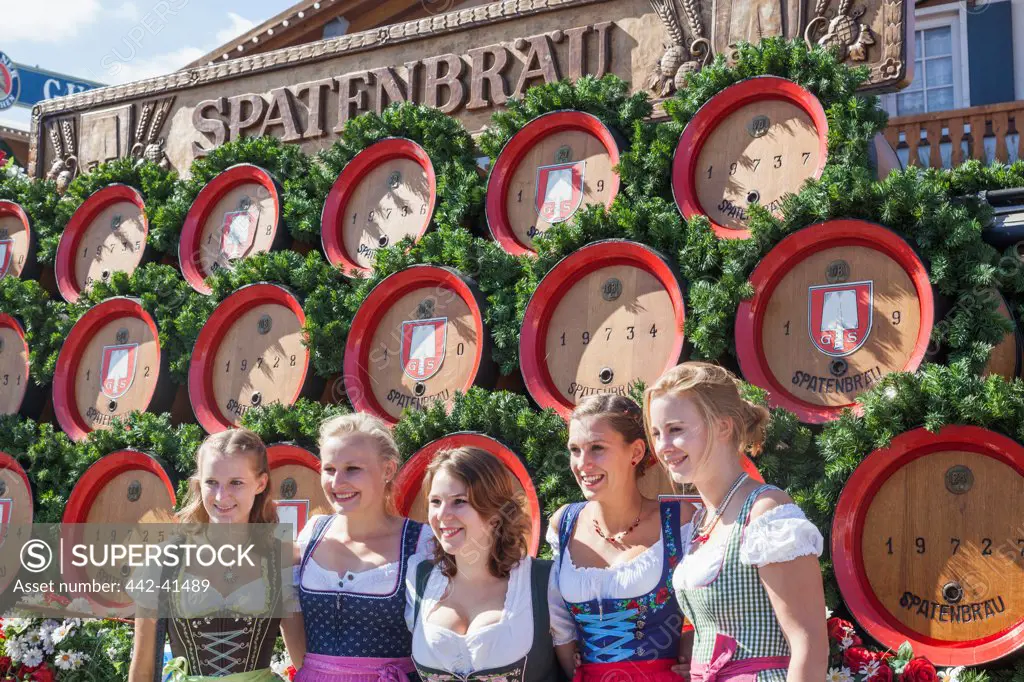 Women dressed in Bavarian costume posing in front of beer kegs, Oktoberfest, Munich, Bavaria, Germany