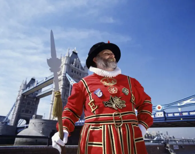 Low angle view of a Beefeater standing with a bridge in the background, Tower Bridge, London, England