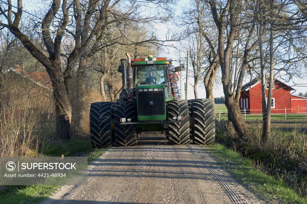 John Deere 9400 tractor, with dual wheels, driving along small road on way to fields, Uppland, Sweden, may