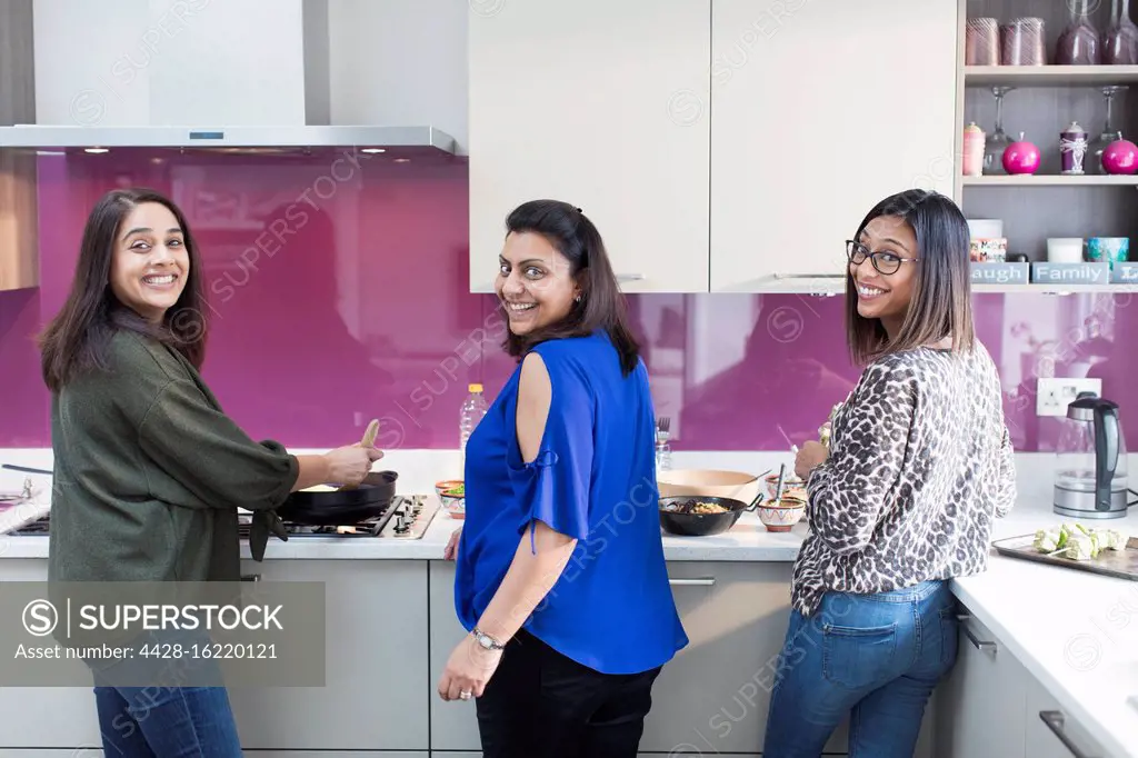 Portrait happy Indian sisters cooking food in kitchen