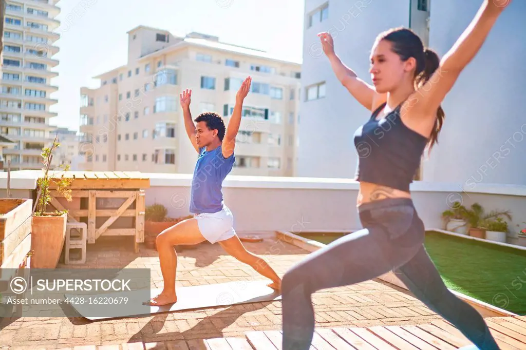 Young couple practicing yoga on sunny urban rooftop balcony