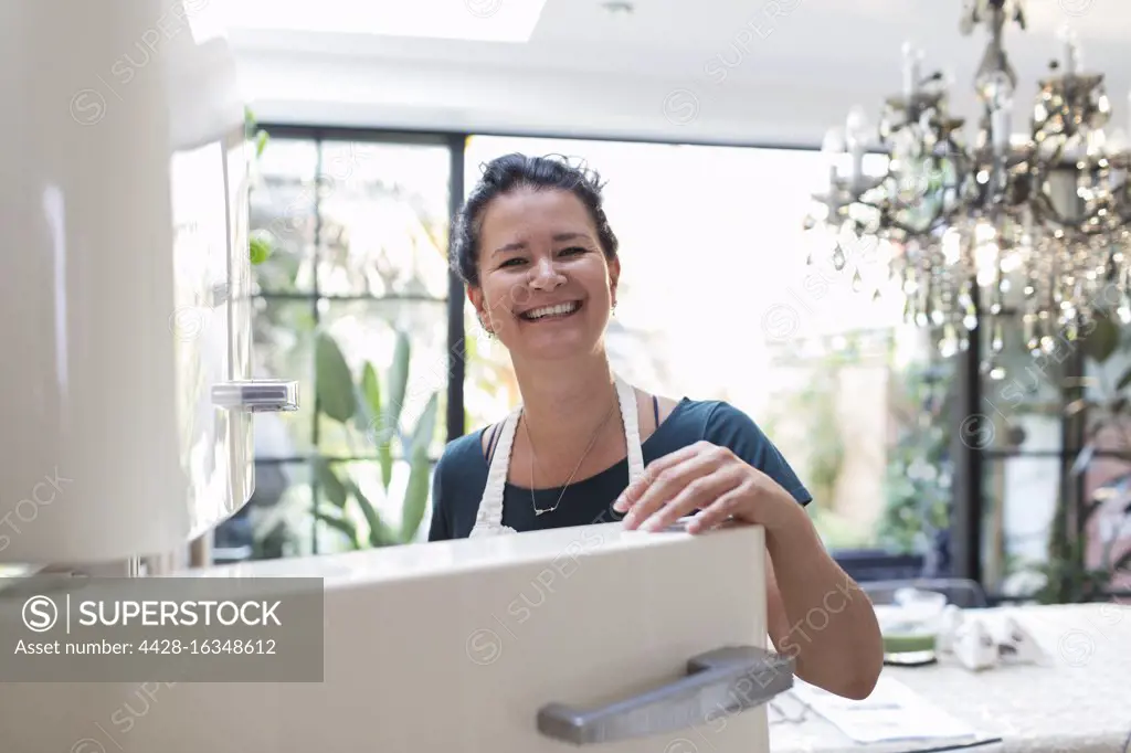 Portrait happy woman at open refrigerator in kitchen