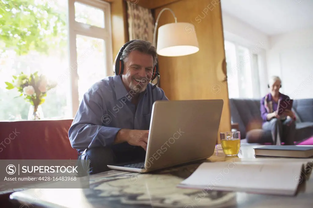 Happy senior man with headphones using laptop in living room