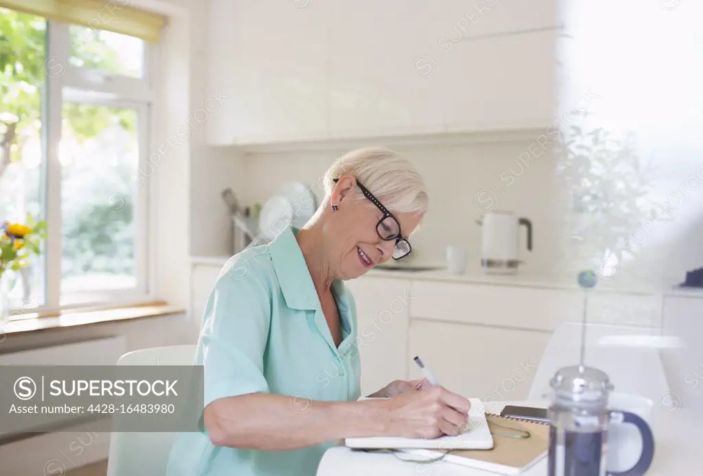 Senior woman writing in journal at morning kitchen table