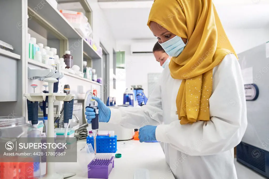 Female scientist in hijab and face mask using pipette in laboratory