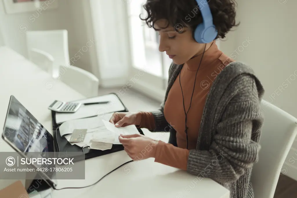 Woman with headphones and receipts paying bills at digital tablet