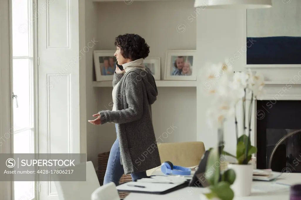 Woman working from home talking on smart phone at window