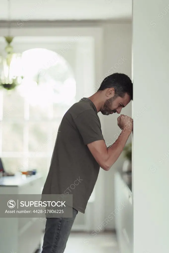 Frustrated man with clenched fists leaning against wall