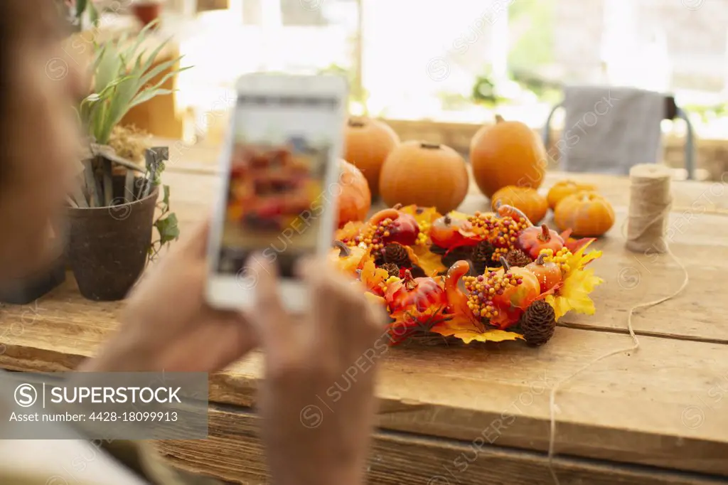 Florist with camera phone photographing autumn display in shop