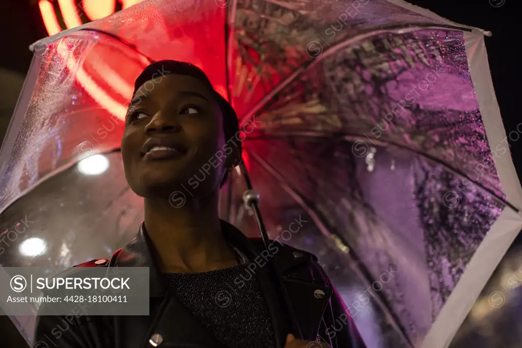 Smiling young woman under umbrella and neon sign at night