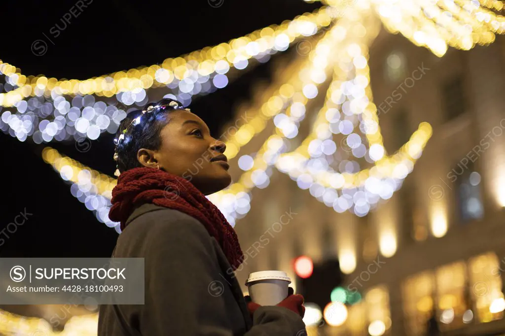 Serene young woman with coffee in city with lights at night