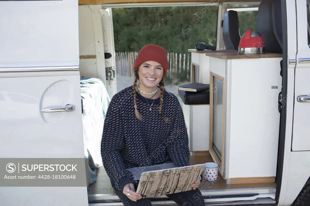 Portrait happy young woman with laptop in camper van doorway