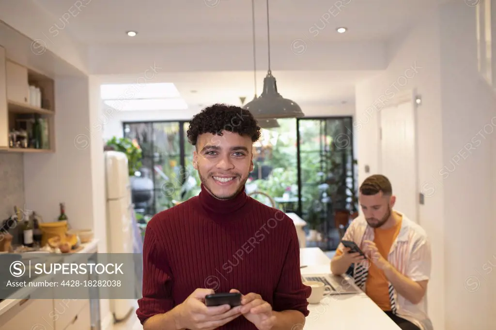 Portrait happy confident young man using smart phone in kitchen