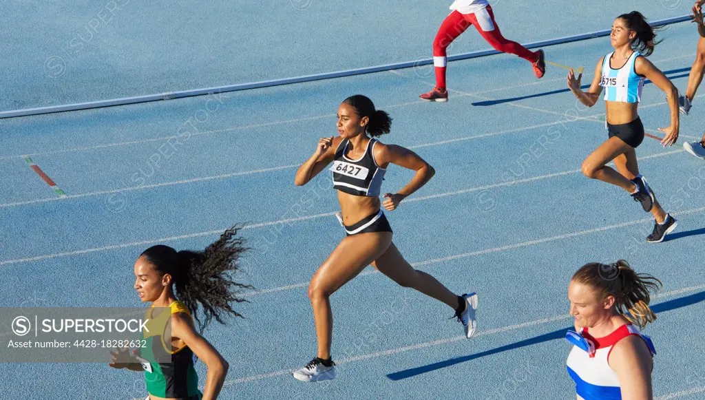 Female track and field athletes running in competition on blue track